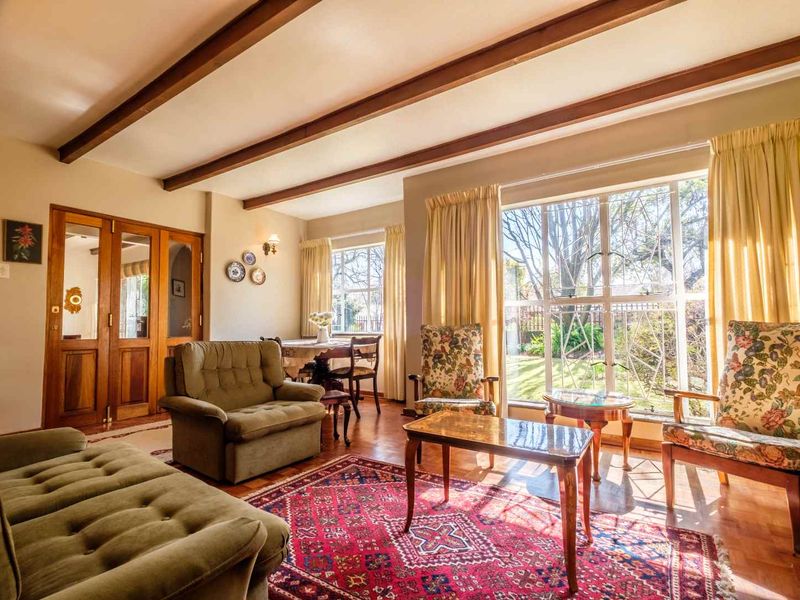 Spacious living room featuring classic parquet flooring, exposed timber ceiling beams, and large windows that provide ample natural light and garden views.