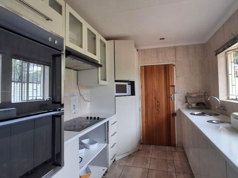 A functional kitchen featuring white cabinetry, built-in oven, electric hob, and double sink with tiled finishes throughout.