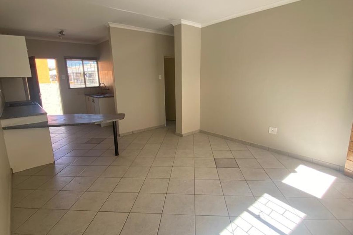 Open plan living and kitchen area featuring tiled flooring, built-in cabinetry, and a breakfast bar, offering a functional and versatile living space.