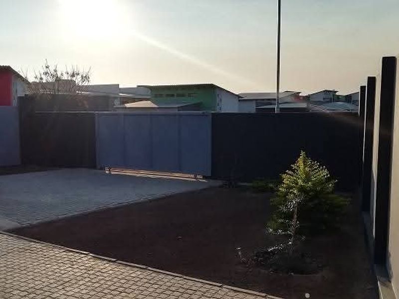 Front exterior view featuring a paved driveway, secure boundary wall, and a sliding gate entrance.