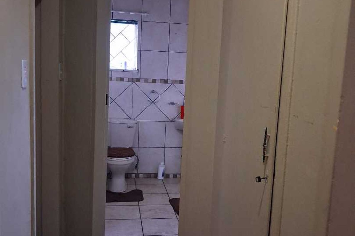A view from a hallway into a small bathroom featuring tiled walls and flooring, a standard toilet, and a basin.