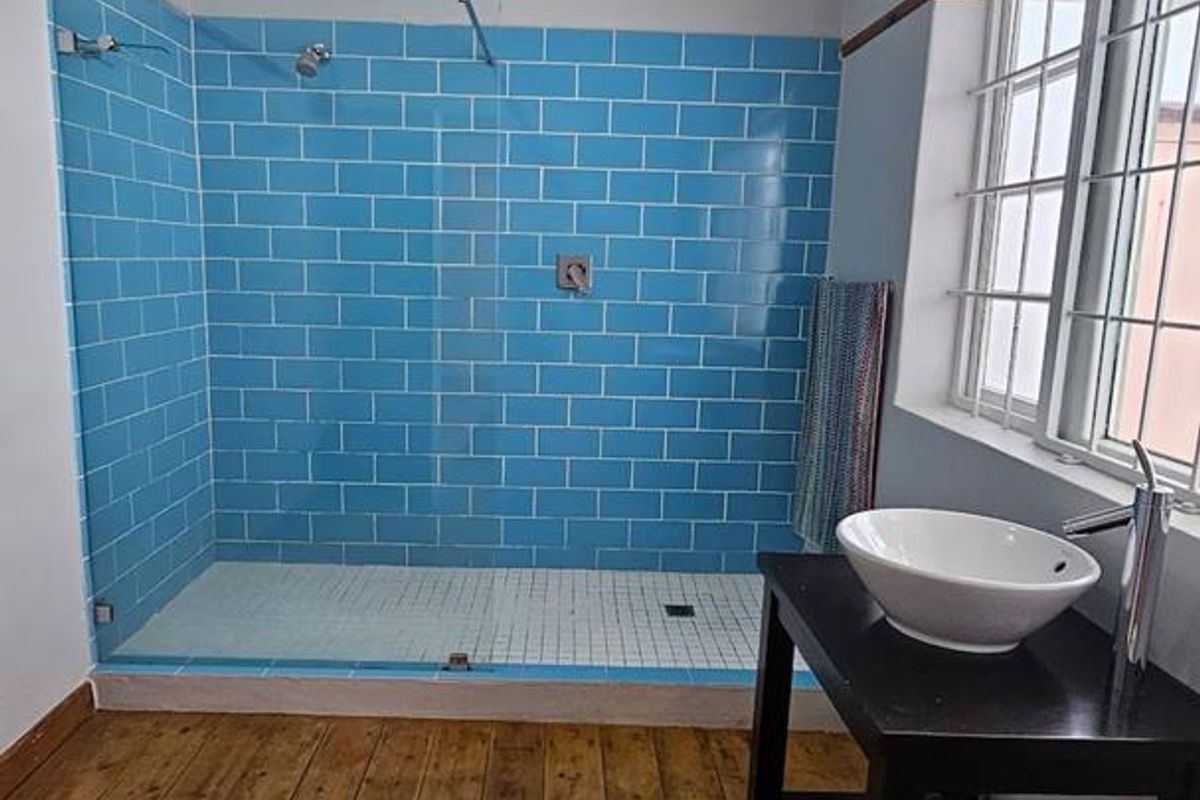 Bathroom featuring a walk-in shower with blue subway tiles, a white vessel sink on a vanity, and timber flooring.