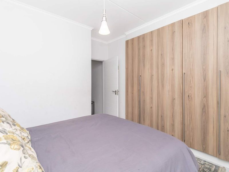 A well-maintained bedroom featuring floor-to-ceiling built-in wooden cupboards and a simple pendant light fixture.