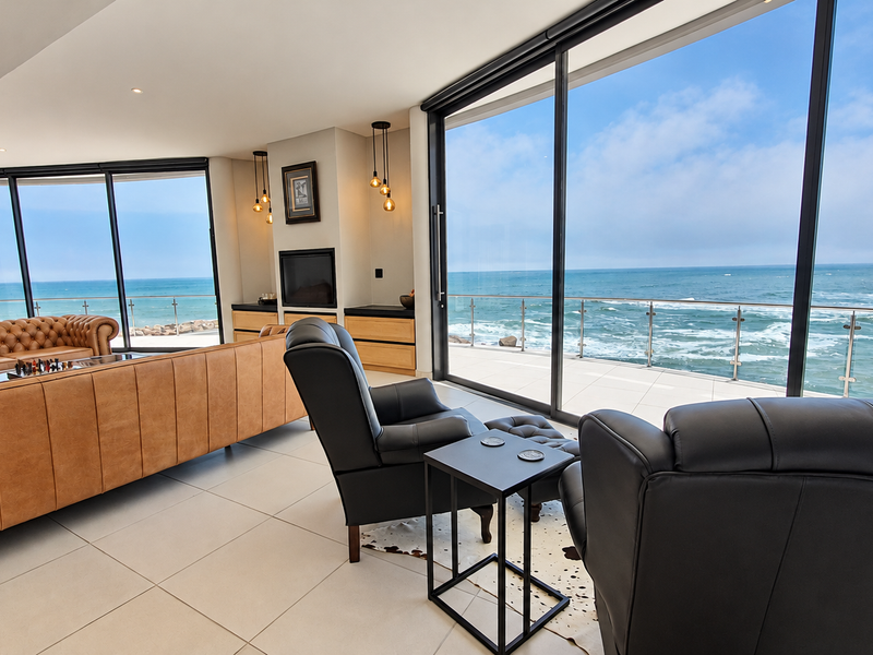 Spacious penthouse living area featuring floor-to-ceiling sliding glass doors that open to a balcony with panoramic ocean views and modern tiled flooring.