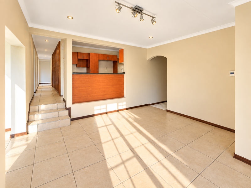 Spacious open-plan living area featuring tiled floors, a kitchen pass-through window, and an arched entryway leading to a hallway.