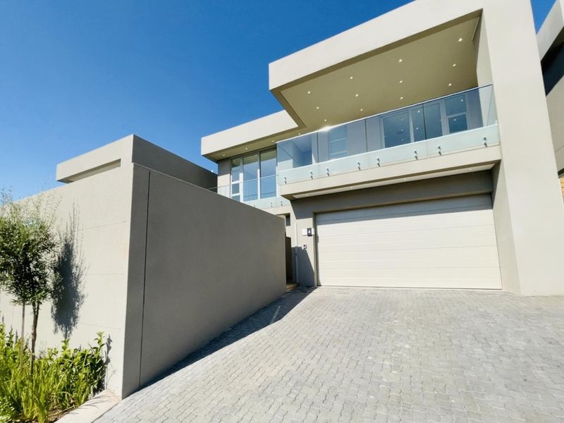 Modern double-story cluster home featuring a paved driveway, automated garage door, and a spacious upper-level balcony with glass balustrades.
