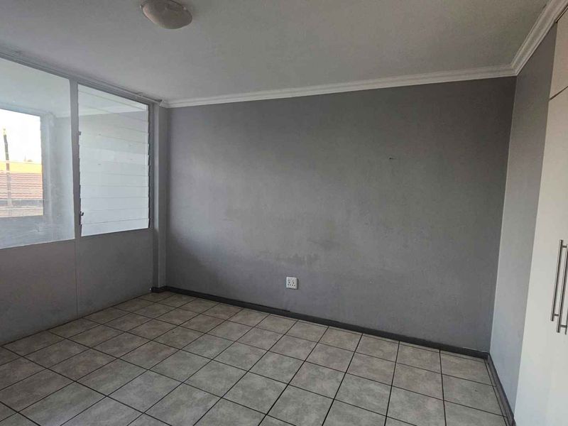 An empty bedroom featuring tiled flooring, built-in cupboards, and an enclosed balcony area, providing a neutral canvas for personalization.