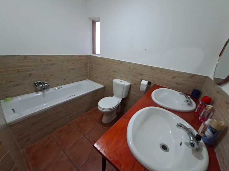 A functional bathroom featuring a bathtub, toilet, and a double vanity with wood-look wall tiling and terracotta floor tiles.