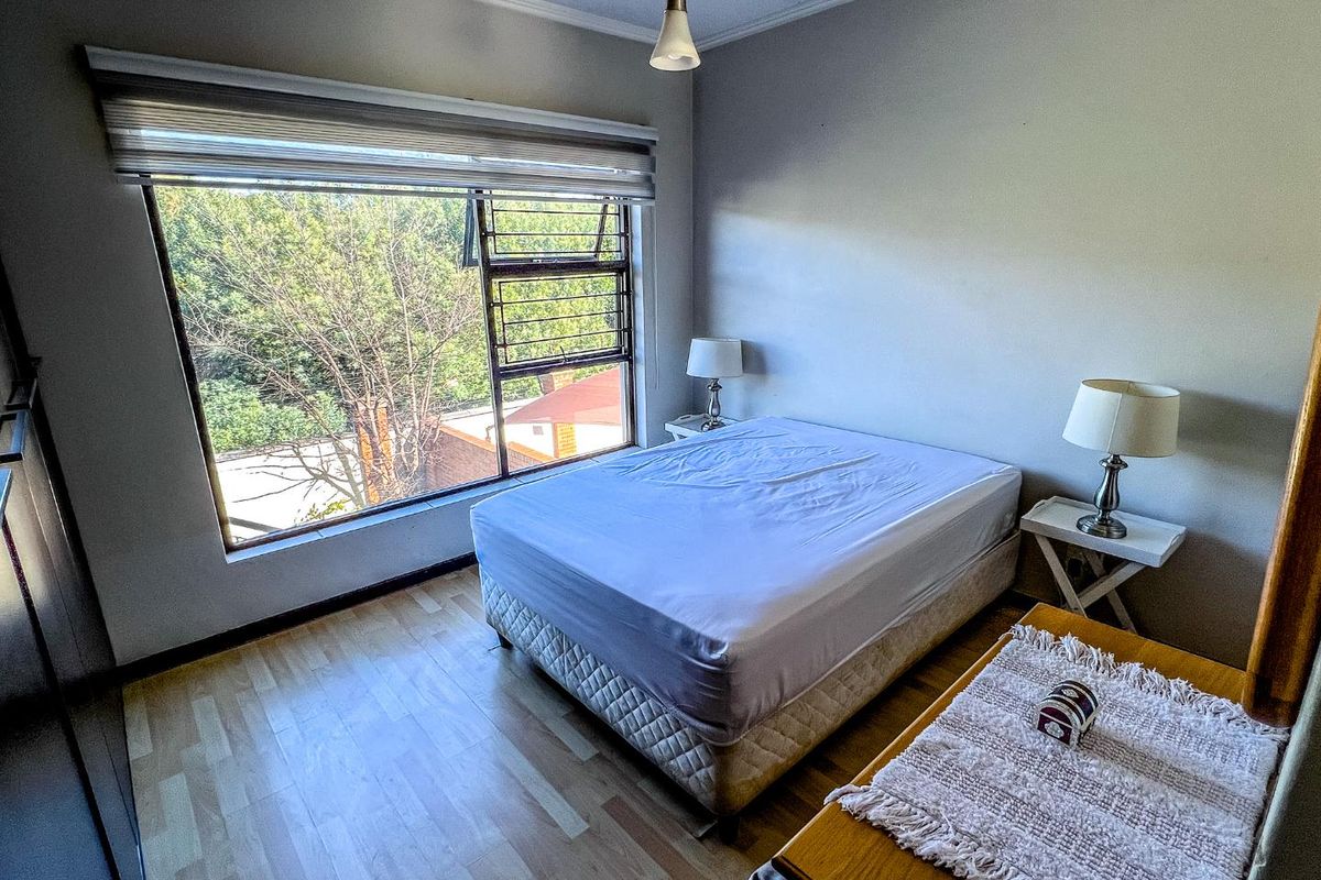 A well-lit bedroom featuring light wood-look flooring, a large window with integrated security bars, and a neutral color palette.
