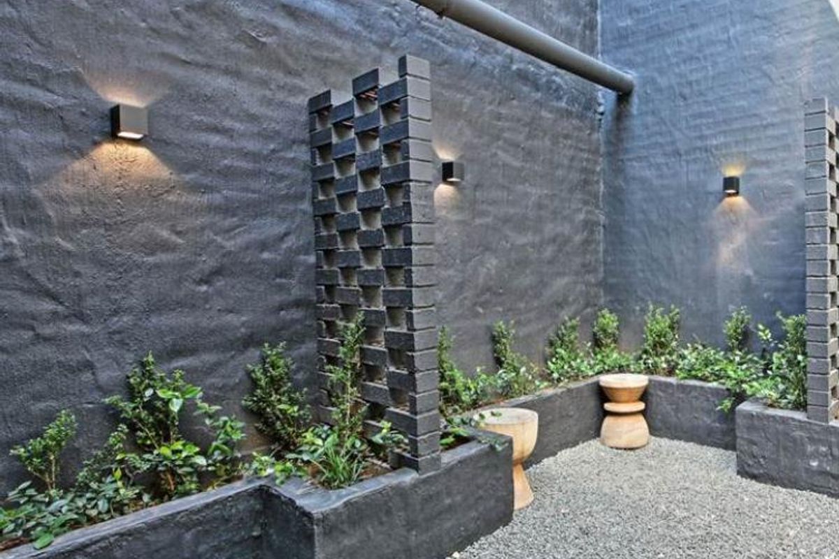 A modern, private courtyard featuring dark-painted textured walls, decorative brick privacy screens, built-in garden planters, and integrated wall-mounted lighting.