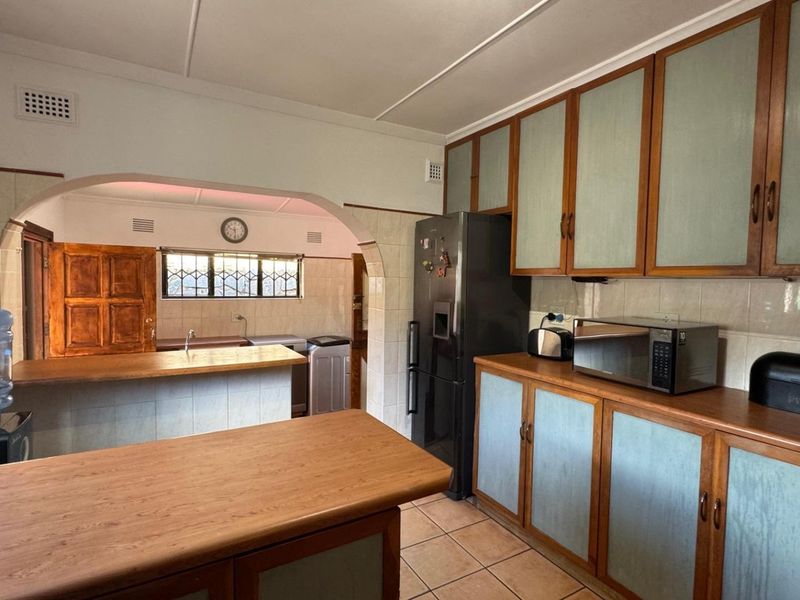 A functional kitchen featuring dated cabinetry, tiled splashbacks, and laminate countertops, with an open-plan layout leading to an adjacent utility area.