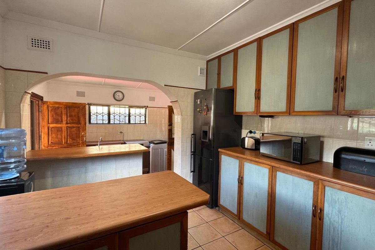 A functional kitchen featuring dated cabinetry, tiled splashbacks, and laminate countertops, with an open-plan layout leading to an adjacent utility area.