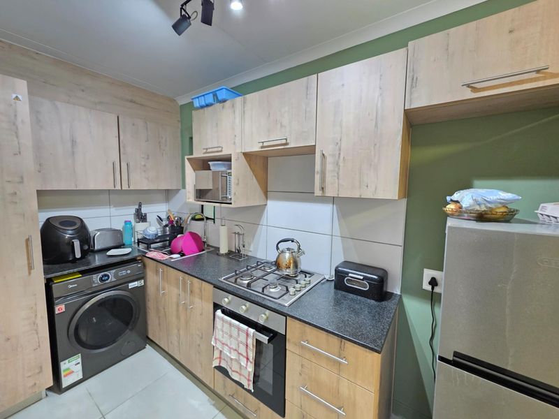 Compact kitchen featuring light wood-look cabinetry, dark countertops, a gas hob, built-in oven, and tiled backsplash with integrated laundry appliance space.