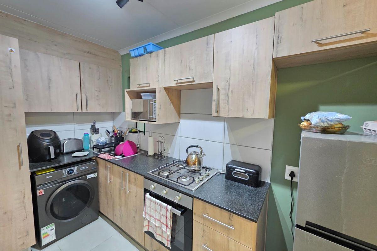 Compact kitchen featuring light wood-look cabinetry, dark countertops, a gas hob, built-in oven, and tiled backsplash with integrated laundry appliance space.
