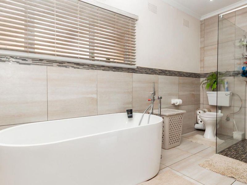 Modern bathroom featuring a sleek freestanding bathtub, a glass-enclosed walk-in shower, and neutral wall tiling with decorative mosaic accents.