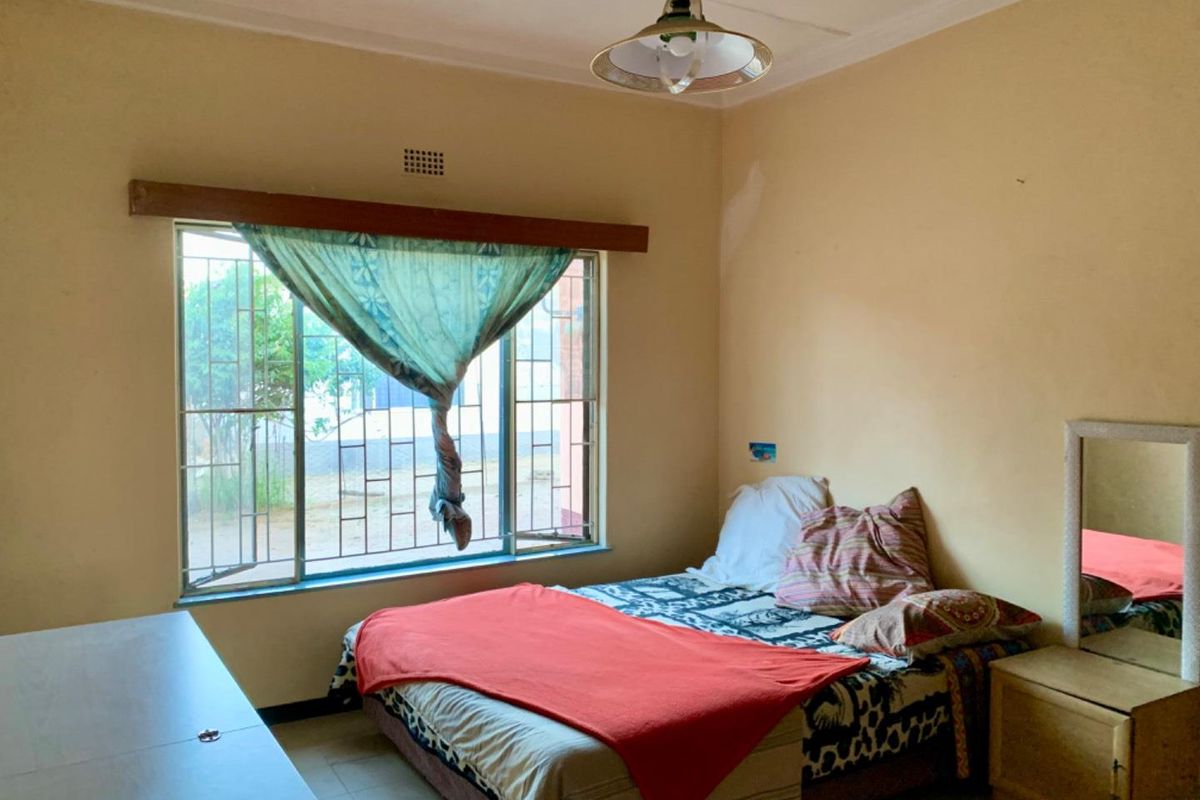 A bedroom featuring a large window with security bars, a ceiling light fixture, and plain wall finishes.