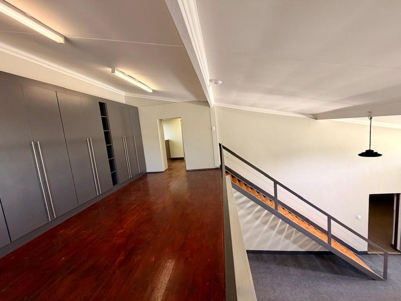 Spacious mezzanine level featuring polished hardwood flooring, extensive built-in cabinetry, and a modern staircase with metal handrails.