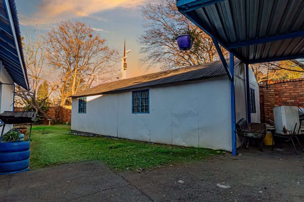 Rear exterior view showing a detached outbuilding with corrugated metal roofing, metal window frames, and an adjacent carport structure.