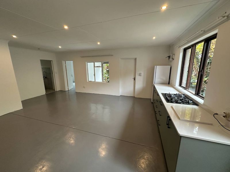 Spacious open-plan kitchen and living area featuring modern epoxy flooring, recessed lighting, and a sleek kitchen counter with a built-in gas hob.