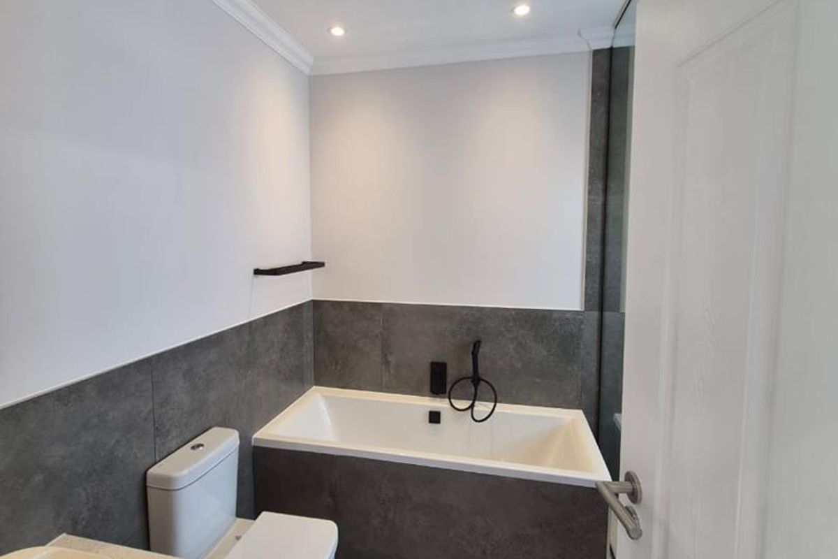 Modern bathroom featuring a built-in bathtub, wall-mounted toilet, vanity with vessel sink, and contemporary grey tiling.