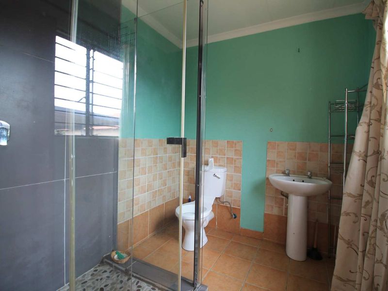 A functional bathroom featuring a pedestal basin, toilet, and a glass-enclosed shower with tiled finishes, requiring cosmetic updates to improve its overall appeal.