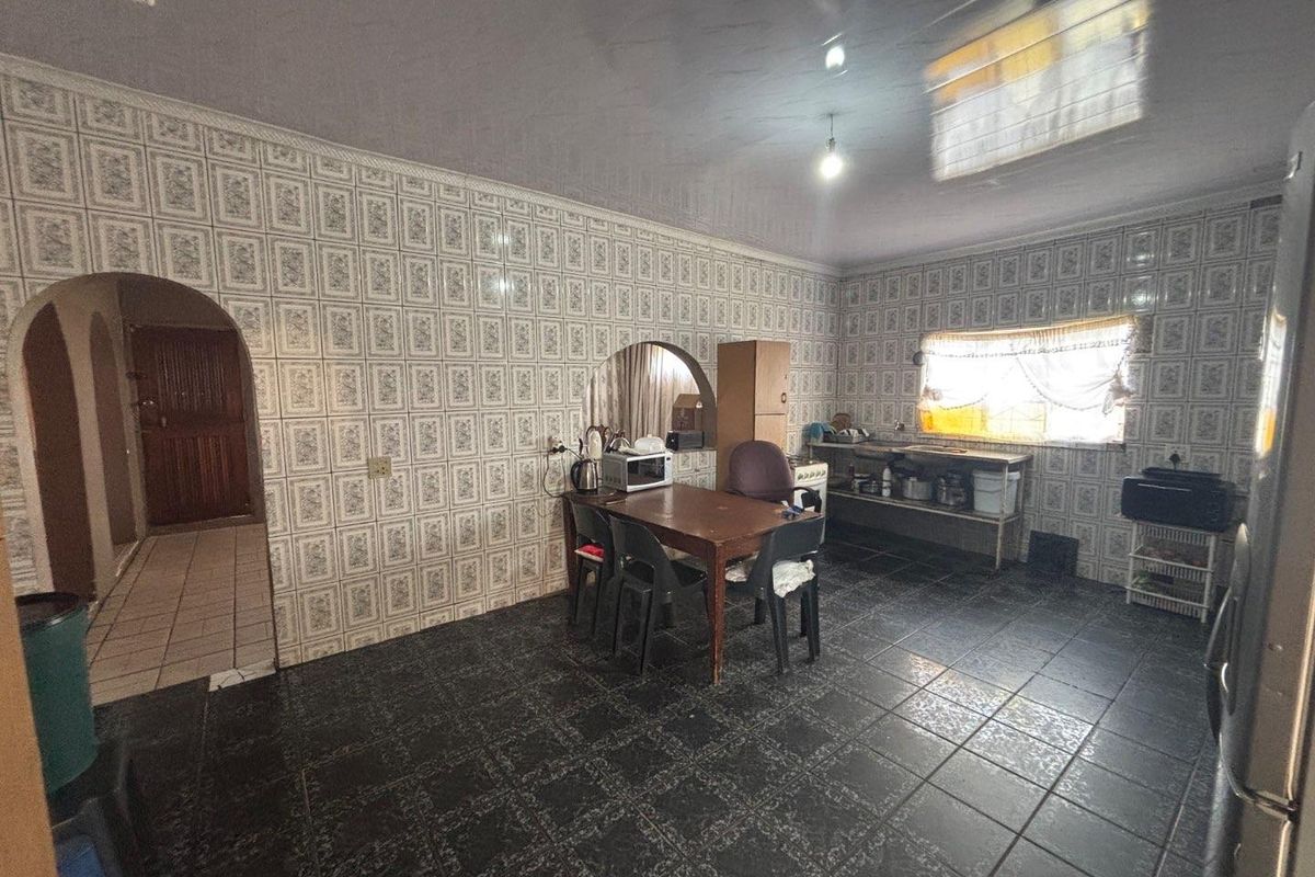 A spacious kitchen area featuring extensive wall tiling, dark floor tiles, and arched doorways, offering a functional layout with potential for modern renovation.