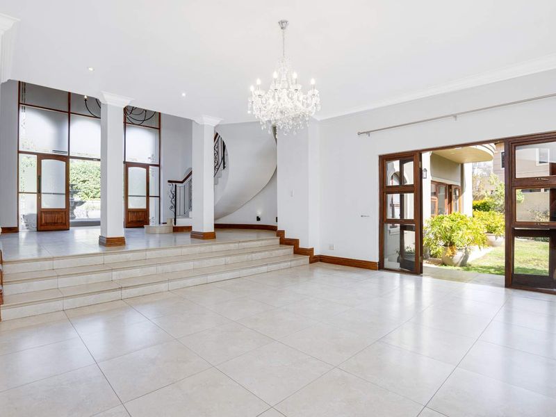 Spacious open-plan living area featuring tiled floors, a grand curved staircase with wrought iron detailing, and large sliding doors leading to the garden.