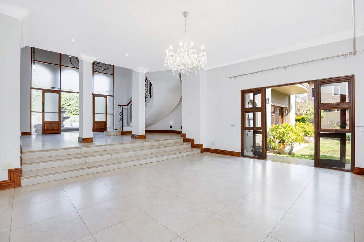 Spacious open-plan living area featuring tiled floors, a grand curved staircase with wrought iron detailing, and large sliding doors leading to the garden.