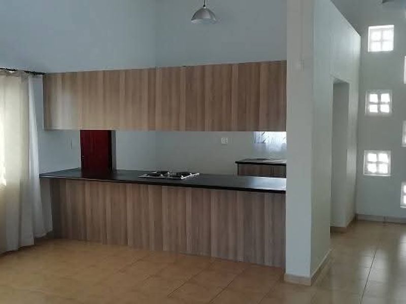 A spacious kitchen area featuring modern wood-finish cabinetry, a built-in hob, tiled flooring, and unique glass block windows providing natural light.