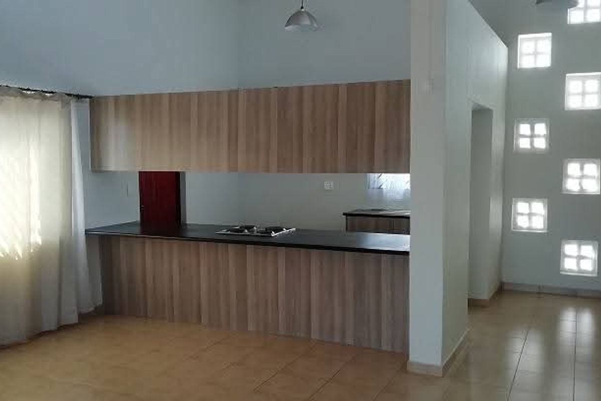 A spacious kitchen area featuring modern wood-finish cabinetry, a built-in hob, tiled flooring, and unique glass block windows providing natural light.