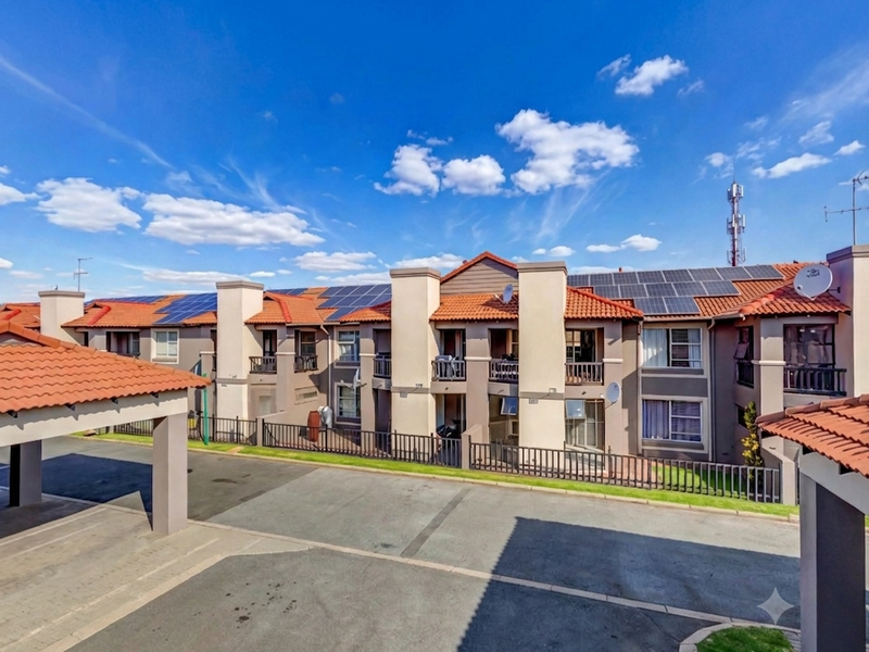 Front elevation of a townhouse complex featuring tiled roofs, solar panel installations, paved driveway, and covered parking areas.