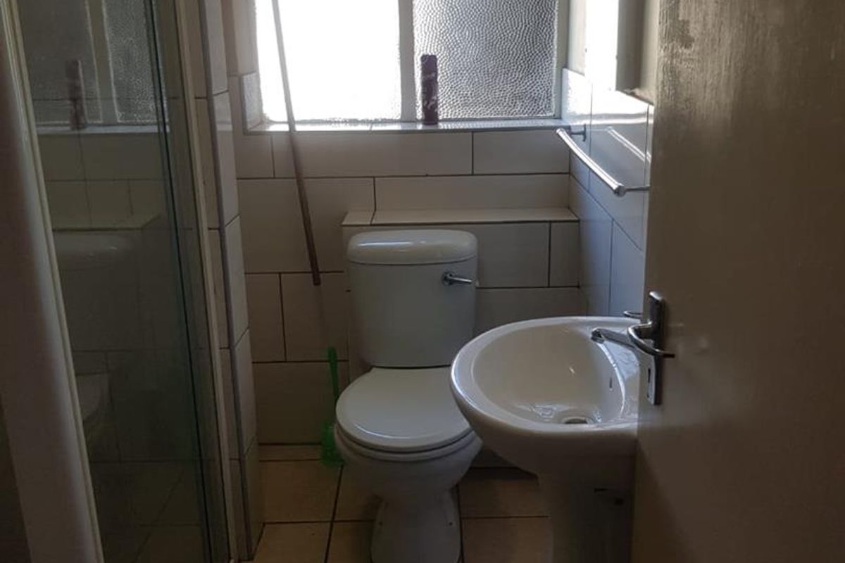 A compact bathroom featuring a pedestal basin, toilet, and shower enclosure with tiled walls and flooring, requiring some cosmetic updates.