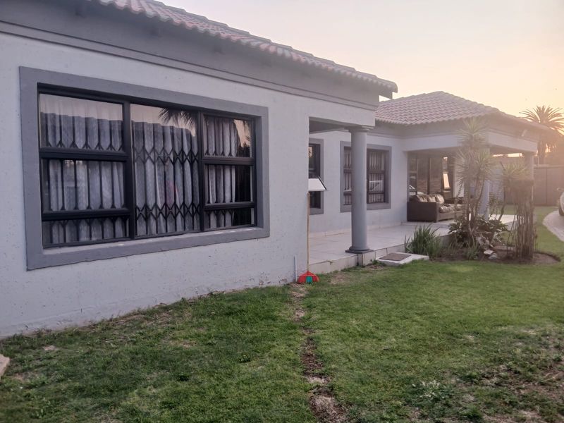 Rear view of the house featuring a covered patio area, tiled roof, and security gates on the windows, set against a landscaped garden.