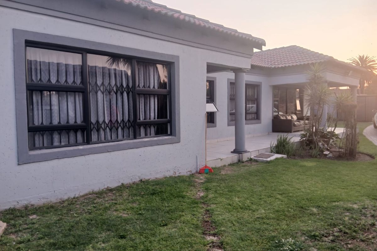 Rear view of the house featuring a covered patio area, tiled roof, and security gates on the windows, set against a landscaped garden.