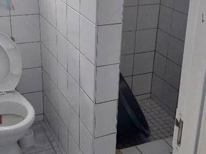 A functional bathroom featuring a tiled shower enclosure and toilet with neutral ceramic floor and wall tiles.