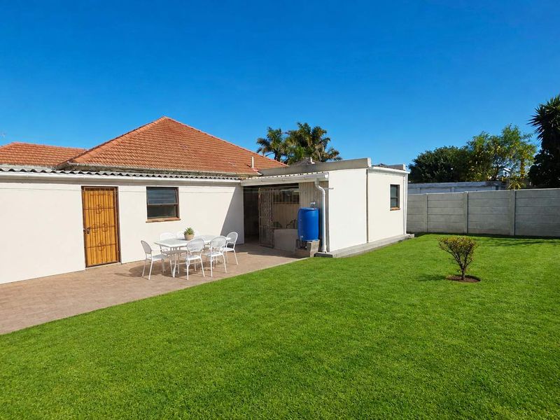 Rear view of the house featuring a paved patio area, a well-maintained lawn, and a secure precast concrete boundary wall.