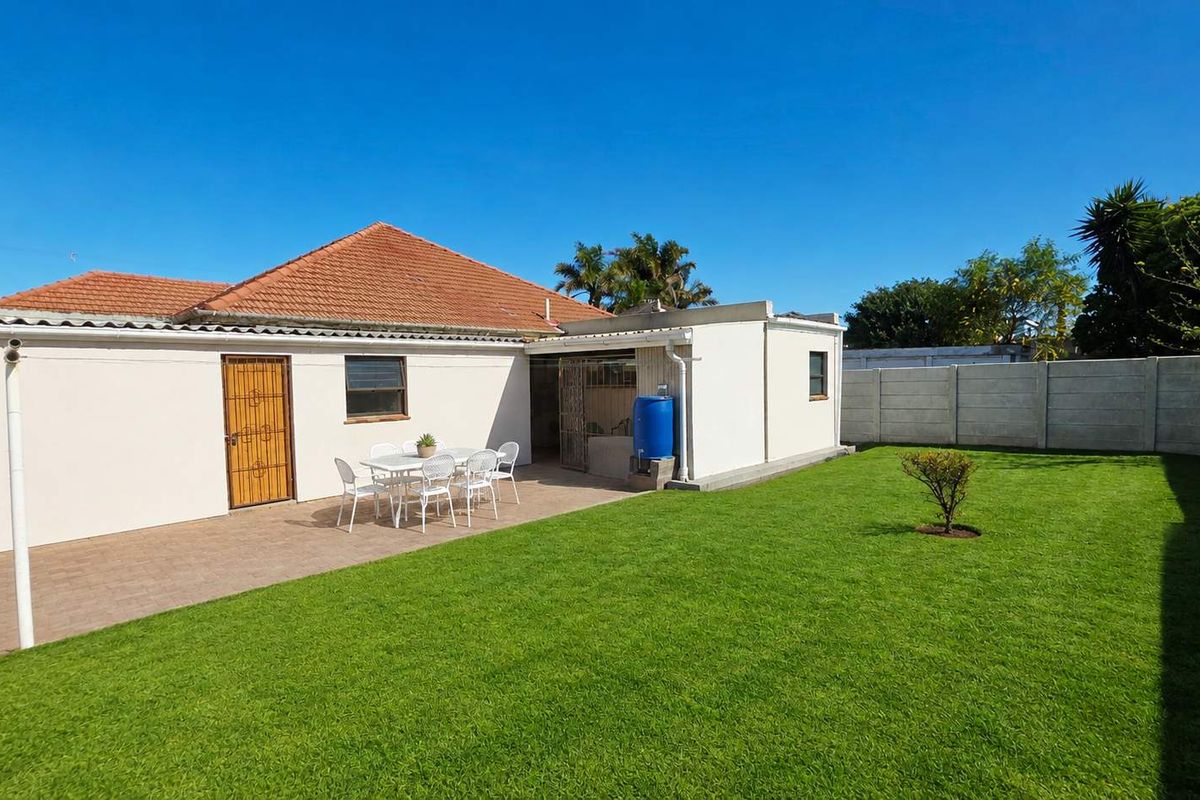 Rear view of the house featuring a paved patio area, a well-maintained lawn, and a secure precast concrete boundary wall.