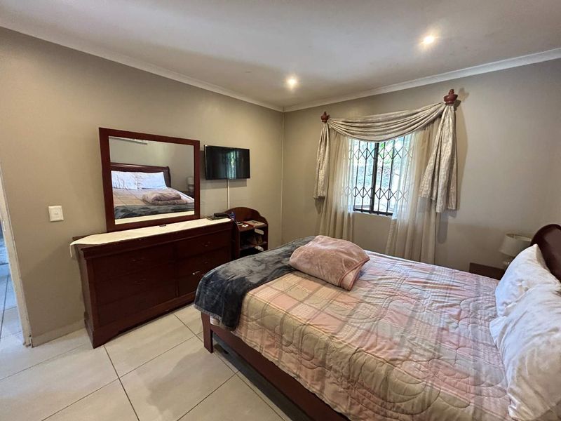 A functional bedroom featuring tiled flooring, recessed downlighting, and a window fitted with a security gate.