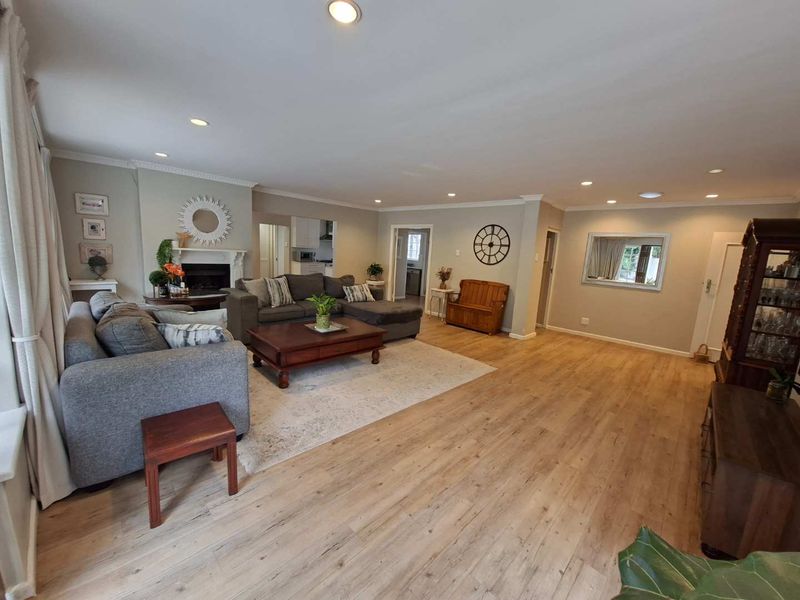 Spacious living room featuring light-toned laminate flooring, recessed lighting, crown molding, and a central fireplace with a classic mantelpiece.