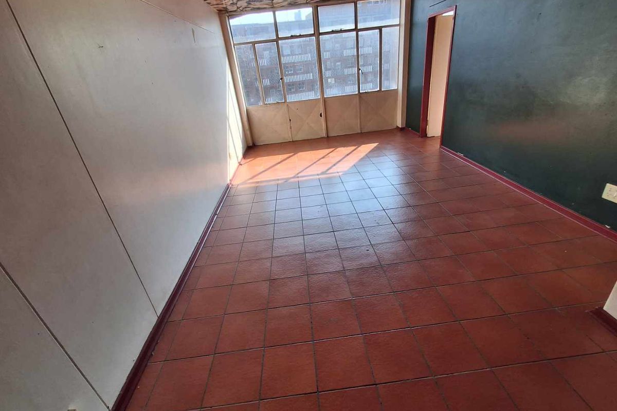 An empty living area featuring red tiled flooring, a large window wall, and a dark accent wall, offering a blank canvas for renovation.