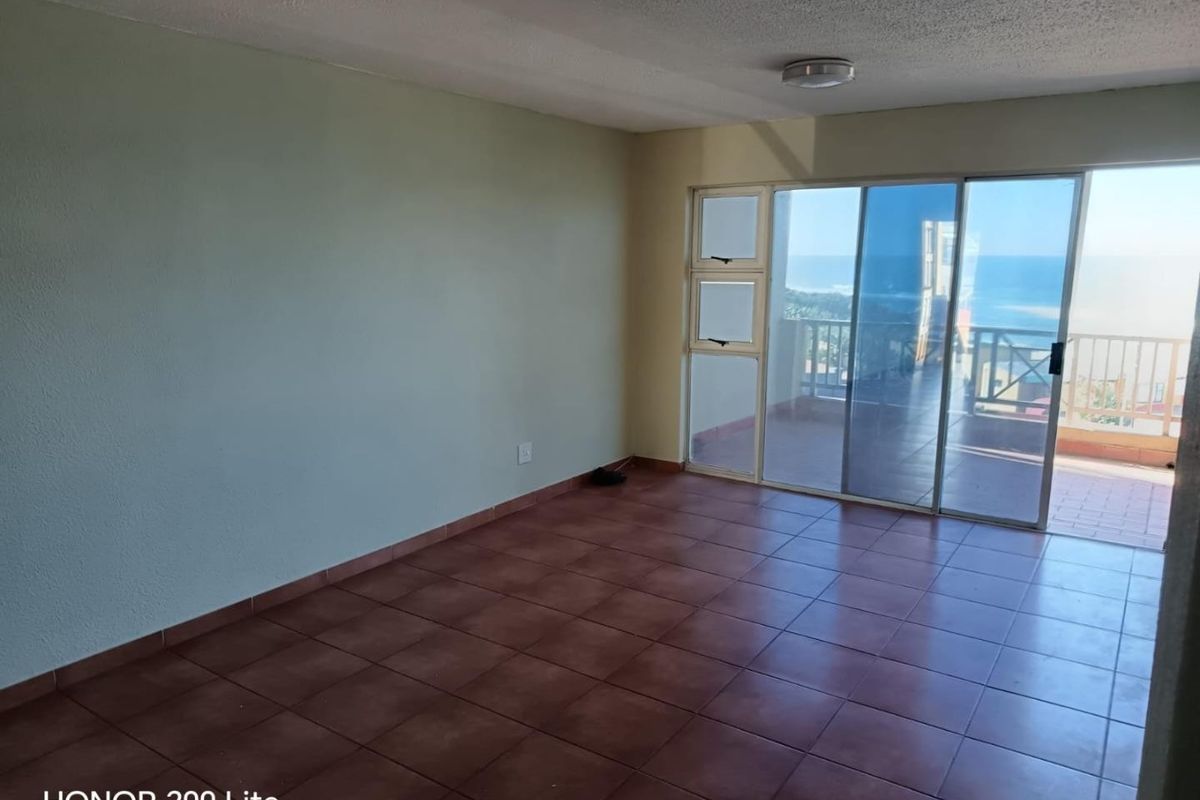 An empty living room featuring tiled flooring and a large sliding glass door that opens onto a balcony with ocean views.
