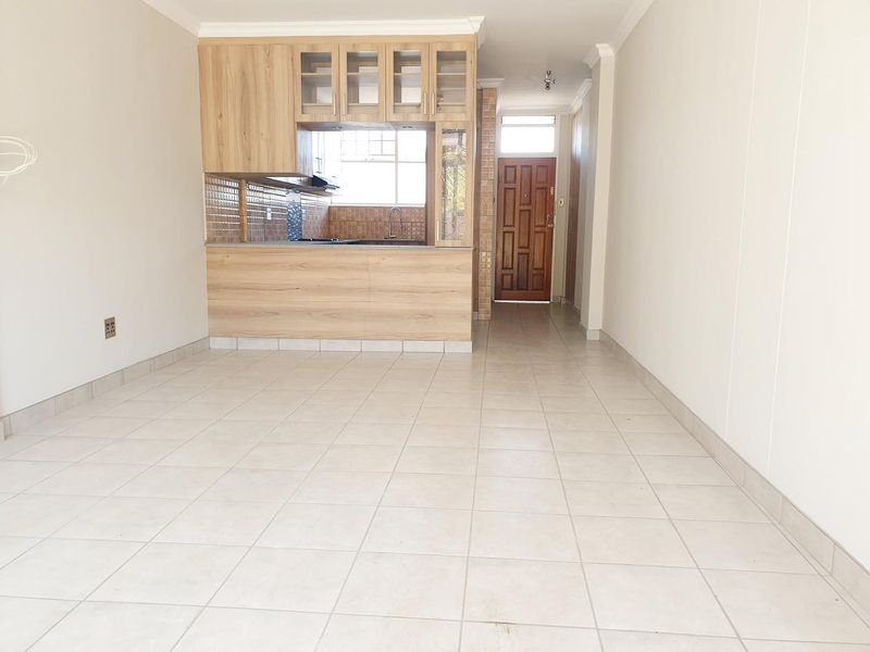 An open-plan living area featuring tiled flooring, a compact kitchen with wooden cabinetry, and a direct view toward the main entrance door.