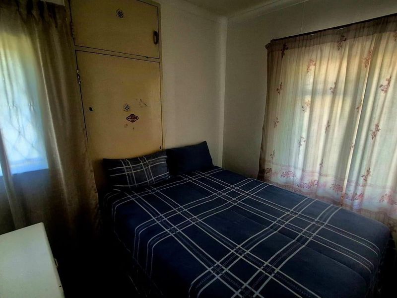 A compact bedroom featuring a built-in cupboard and dual windows, offering a functional space that would benefit from cosmetic updates.