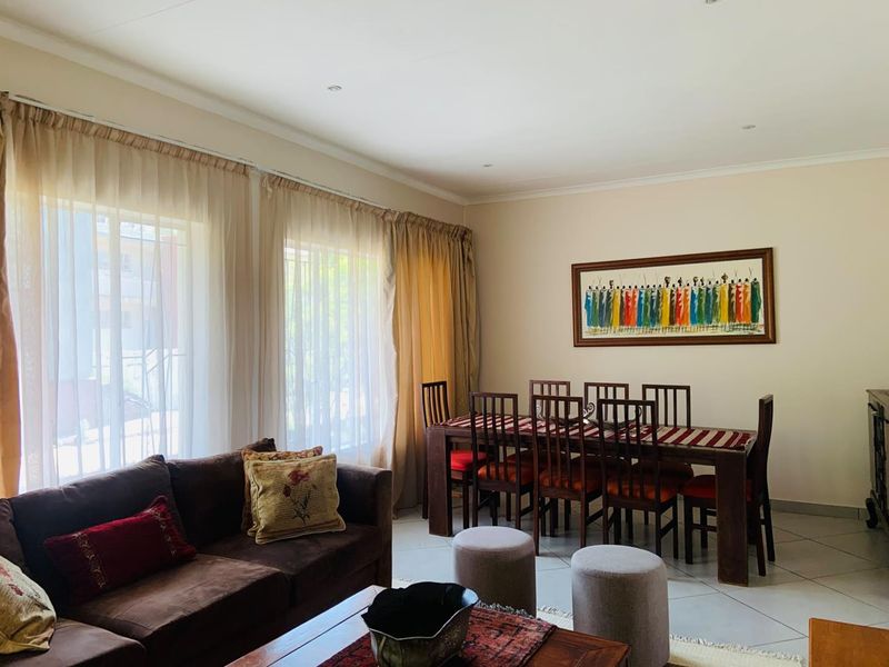 An open-plan living and dining area featuring tiled flooring, recessed lighting, and large windows with curtain tracks.