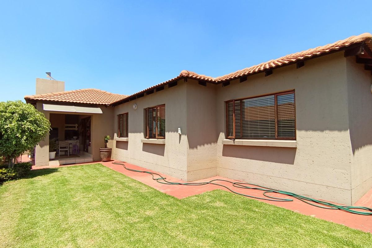 Rear view of the townhouse featuring a covered patio, well-maintained lawn, terracotta roof tiles, and plastered exterior walls.