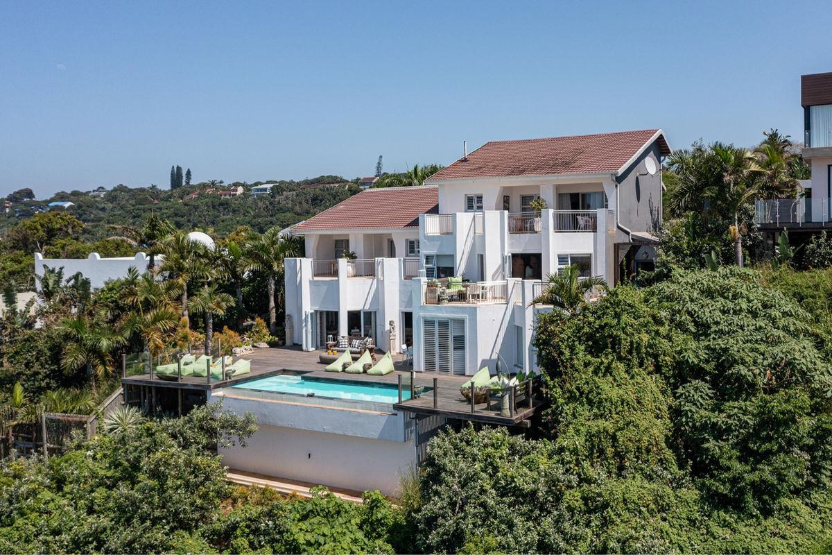 Rear view of a multi-level residence featuring a swimming pool, expansive timber decking, and multiple balconies set within a lush, landscaped environment.