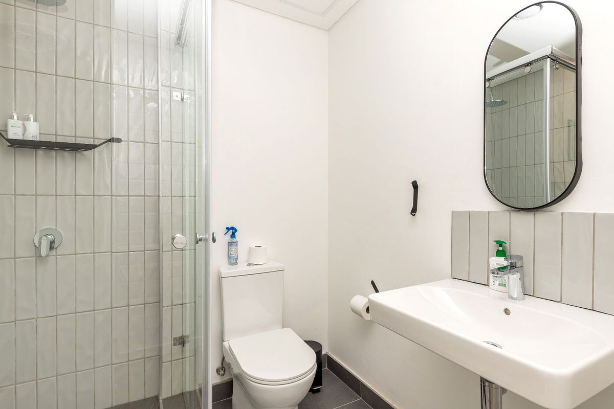A clean, modern bathroom featuring a glass-enclosed shower, pedestal sink with chrome fixtures, and neutral tiling throughout.