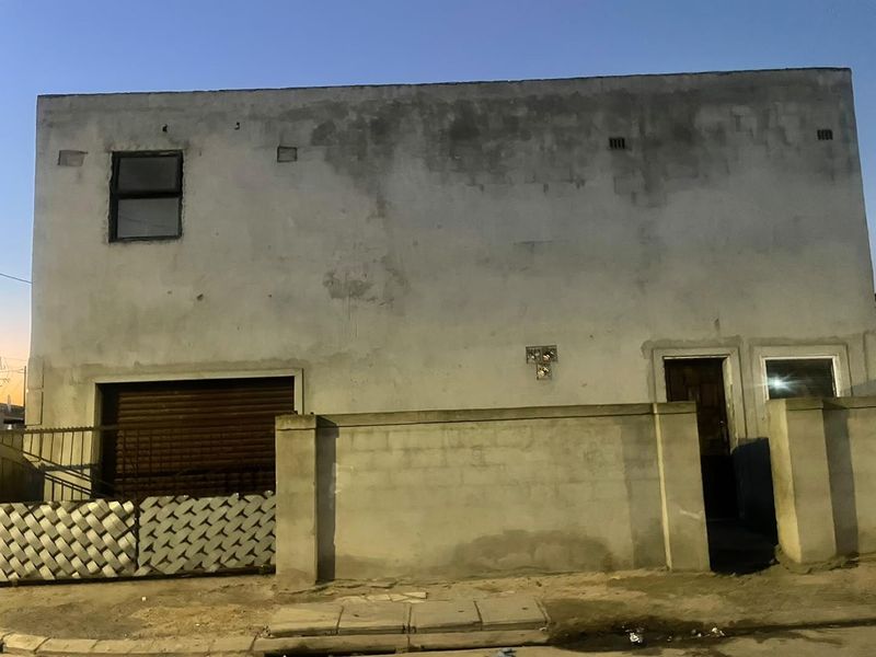 Front elevation of a two-story property featuring a roller shutter garage door, boundary wall, and weathered concrete facade requiring maintenance.