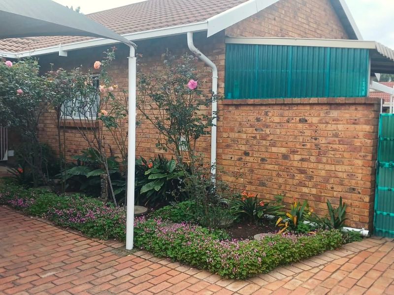 A rear exterior view of a face brick cluster home featuring a paved patio area, shade sail, and established garden beds.