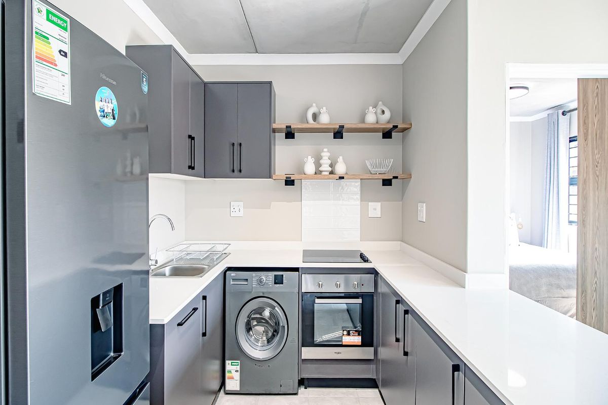 Modern compact kitchen featuring dark grey cabinetry, white stone countertops, built-in oven, electric hob, and integrated laundry appliance space.